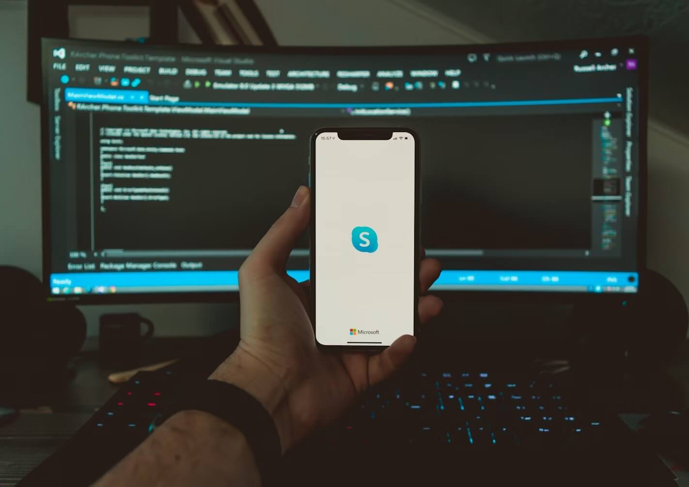 A person's hand holding a mobile phone that displays Skype's splash screen